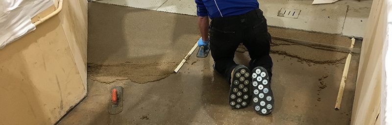 An installer using a trowel to apply a screed on an industrial subfloor.